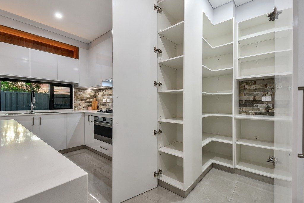 A kitchen with white cabinets and shelves and a pantry.