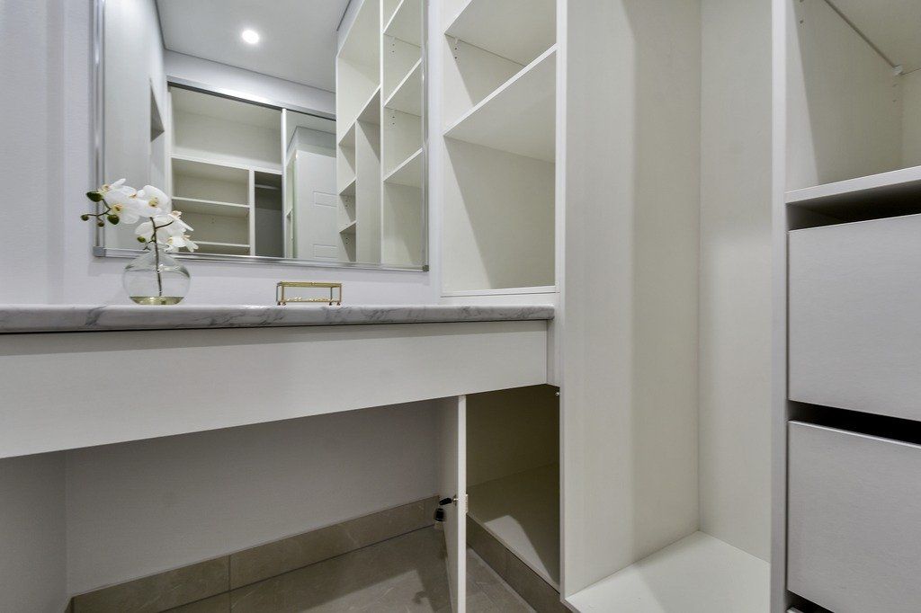 A bathroom with a vanity , mirror , drawers and shelves.