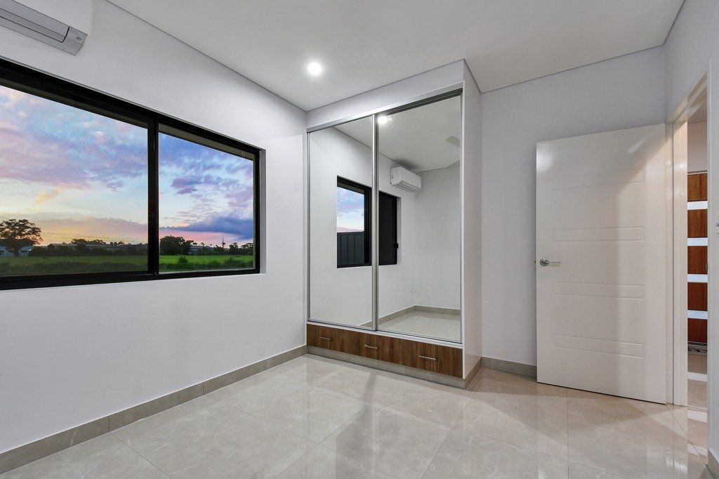 An empty bedroom with a large mirrored wardrobe and two windows.