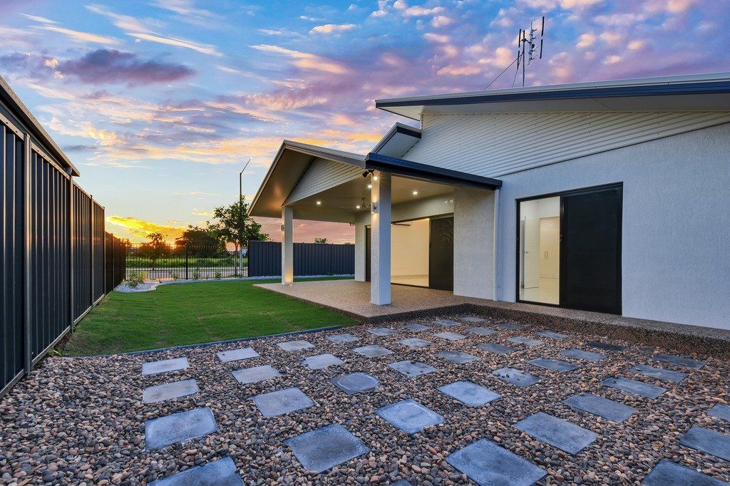 A white house with a covered porch and a gravel driveway in front of it.