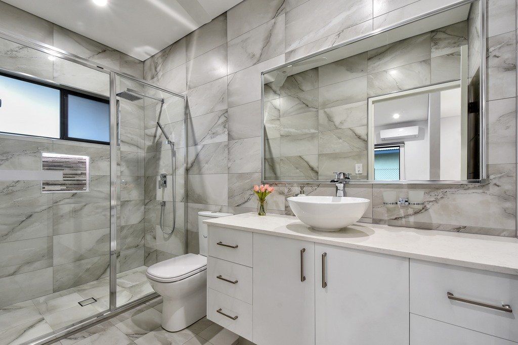A bathroom with a toilet , sink , mirror and walk in shower.