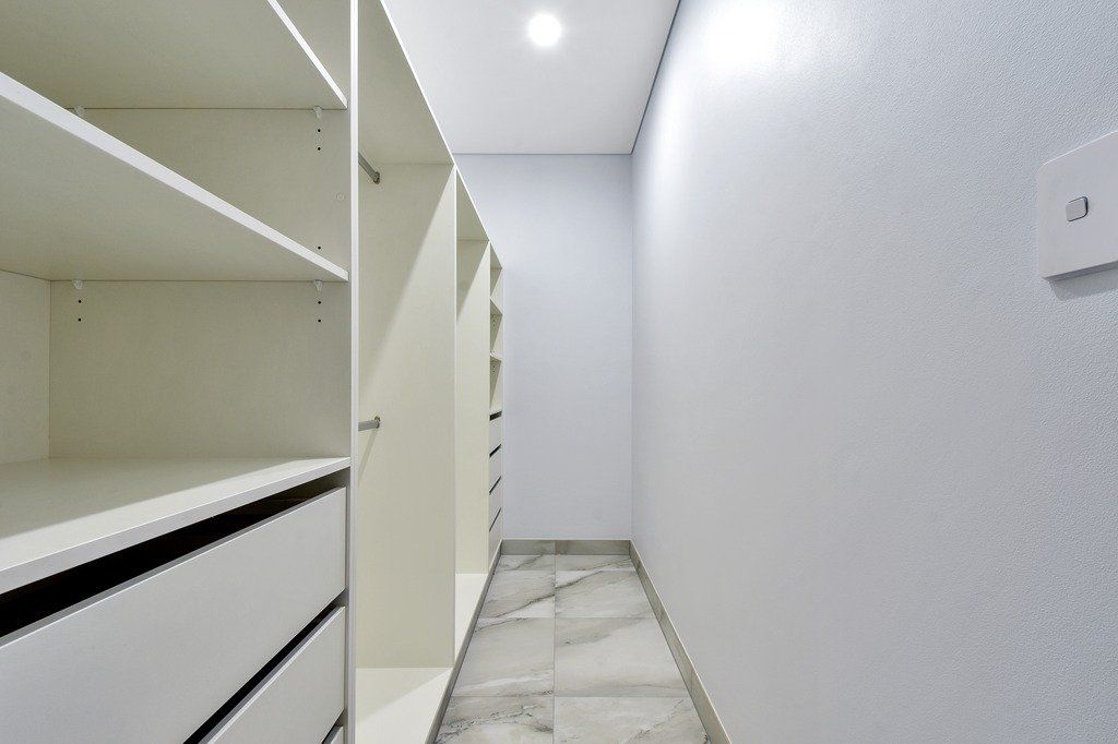 An empty walk in closet with white shelves and drawers.