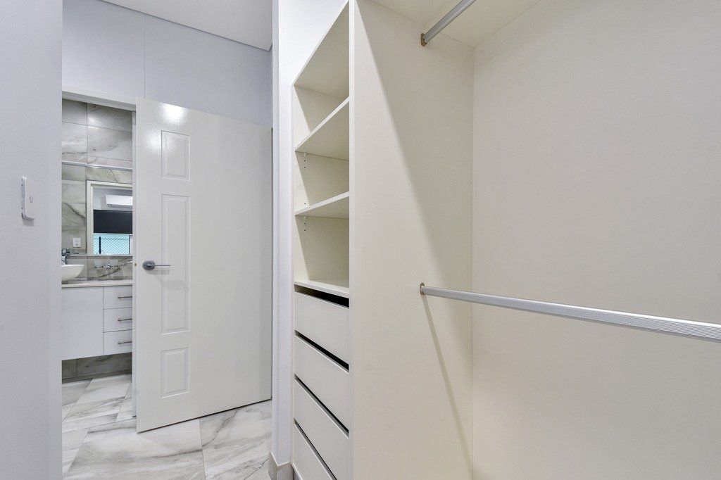 A walk in closet with a bathroom in the background.
