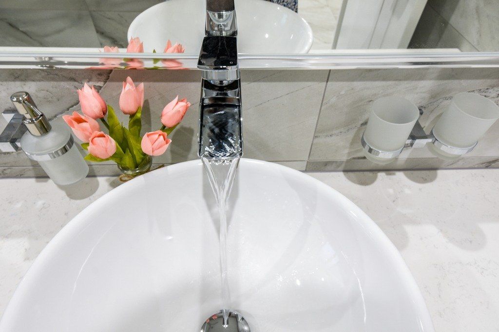 A bathroom sink with water running from a faucet and flowers in a vase.