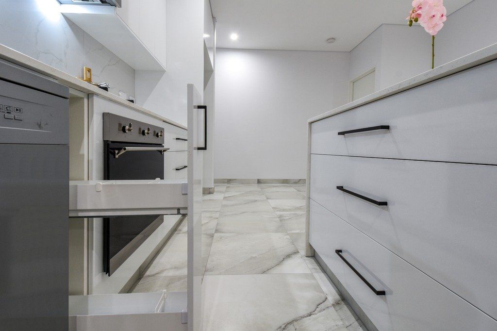 A kitchen with white cabinets and black handles and a dishwasher.