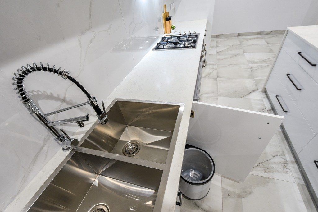 A kitchen with a stainless steel sink , faucet , and trash can.