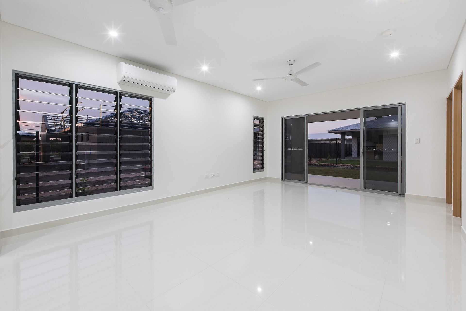 An empty living room with a lot of windows and a ceiling fan.