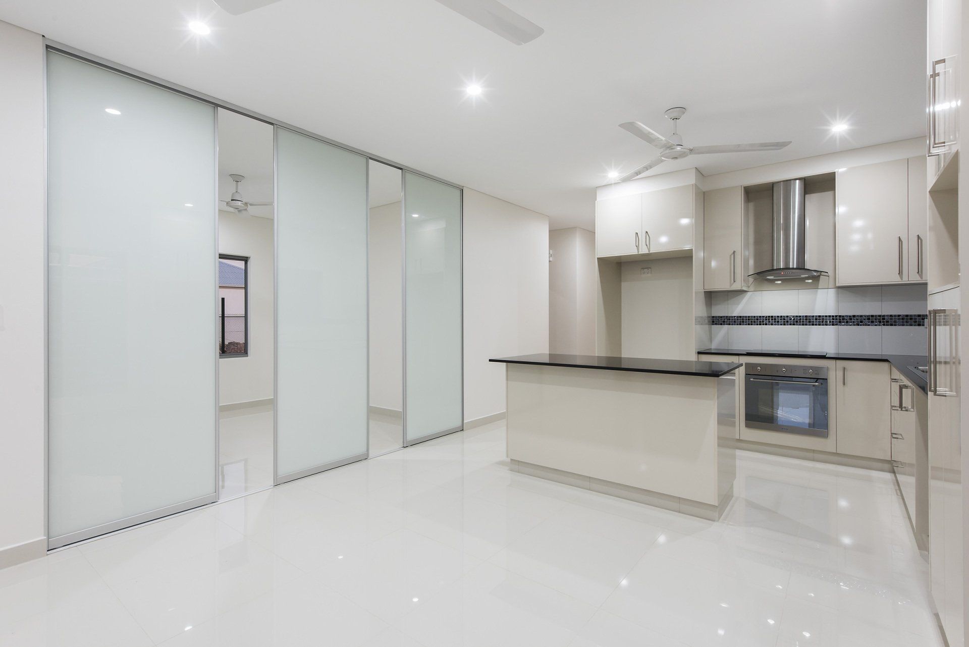 An empty kitchen with white cabinets and sliding glass doors.