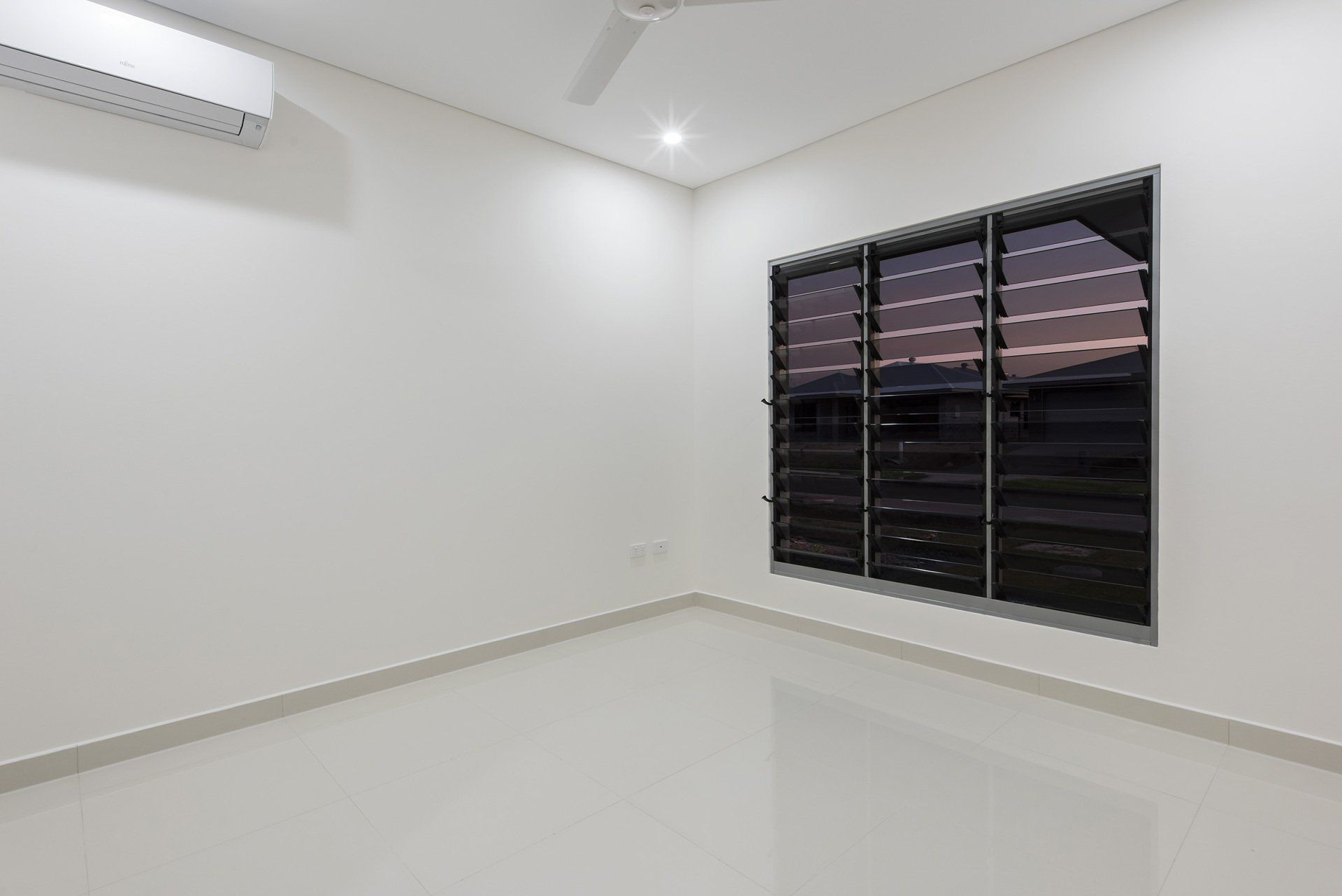 An empty room with two windows and a ceiling fan.