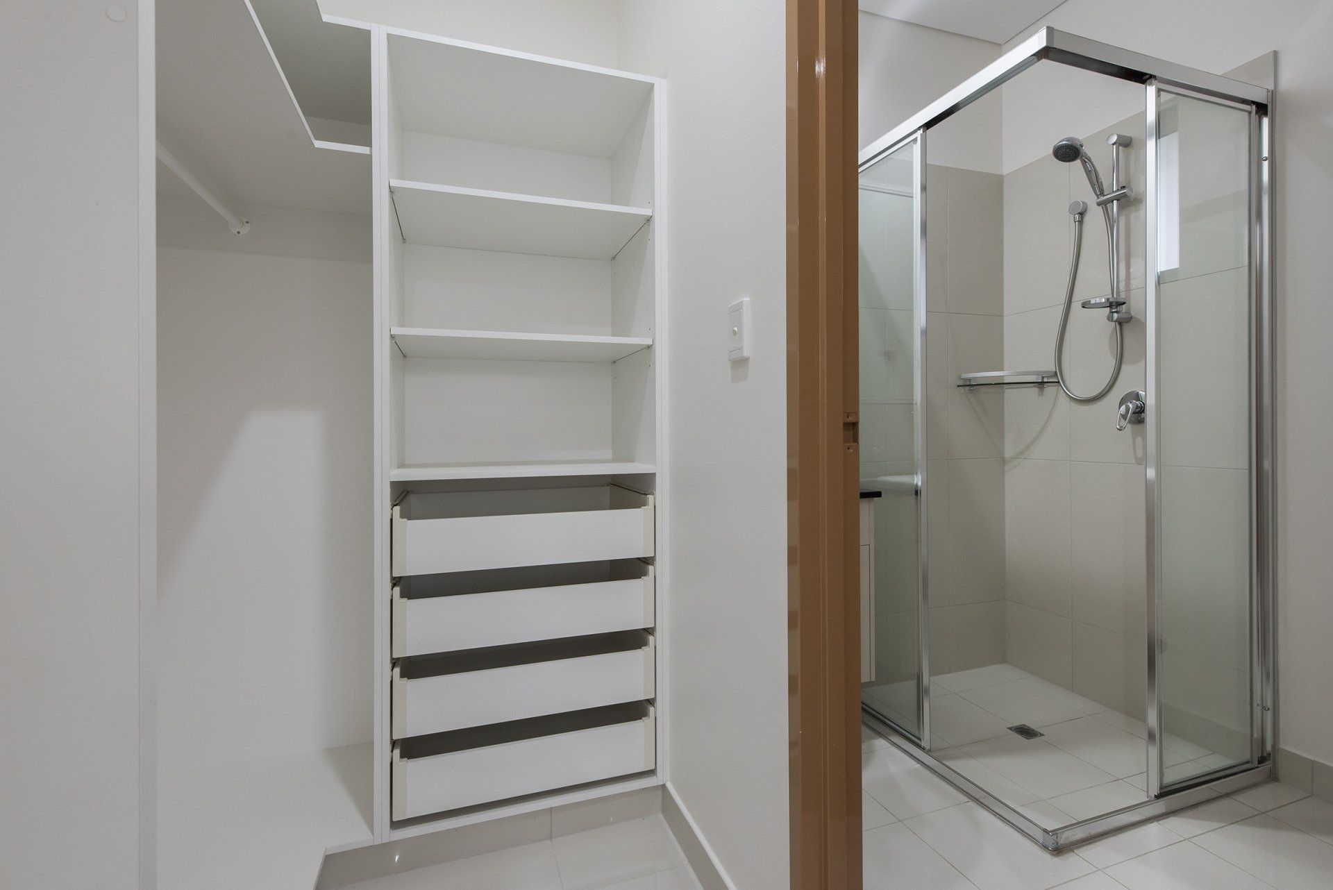 A walk in closet next to a shower with a glass door.