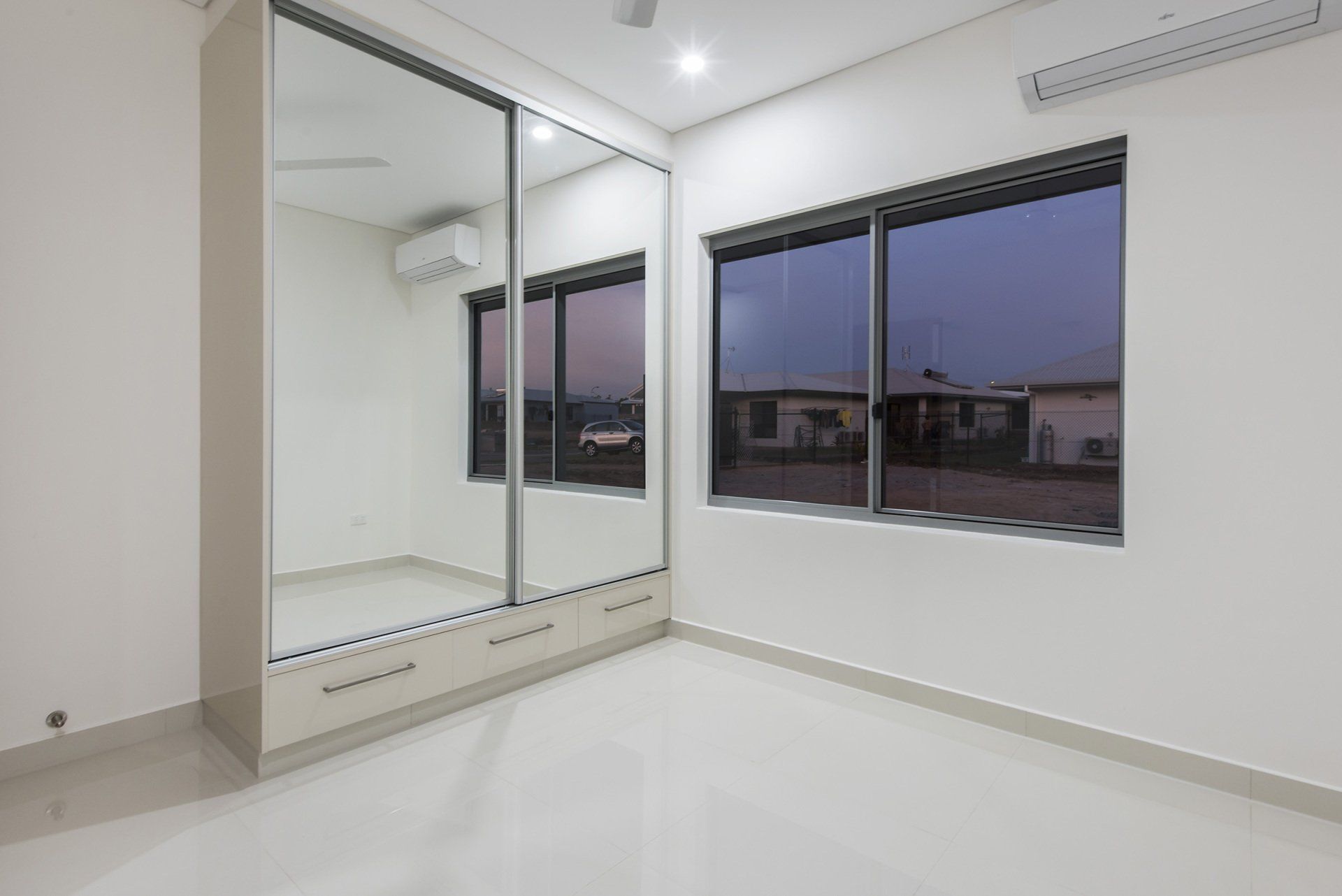A bedroom with a large mirrored wardrobe and two windows.
