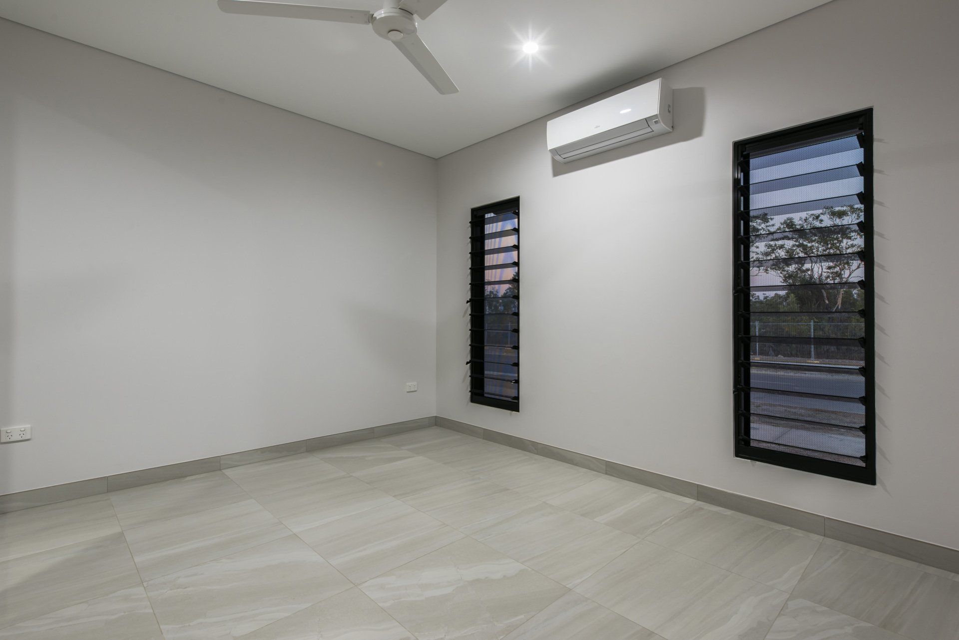 An empty room with two windows and a ceiling fan.