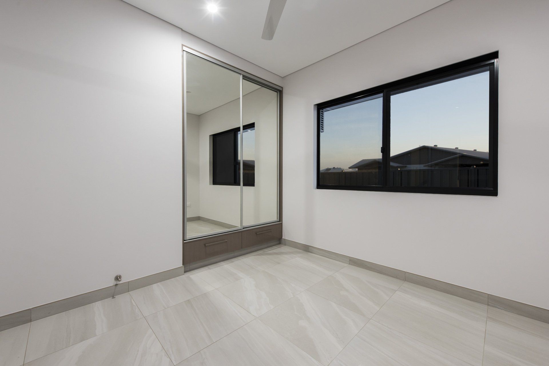 An empty bedroom with a large mirrored wardrobe and two windows.
