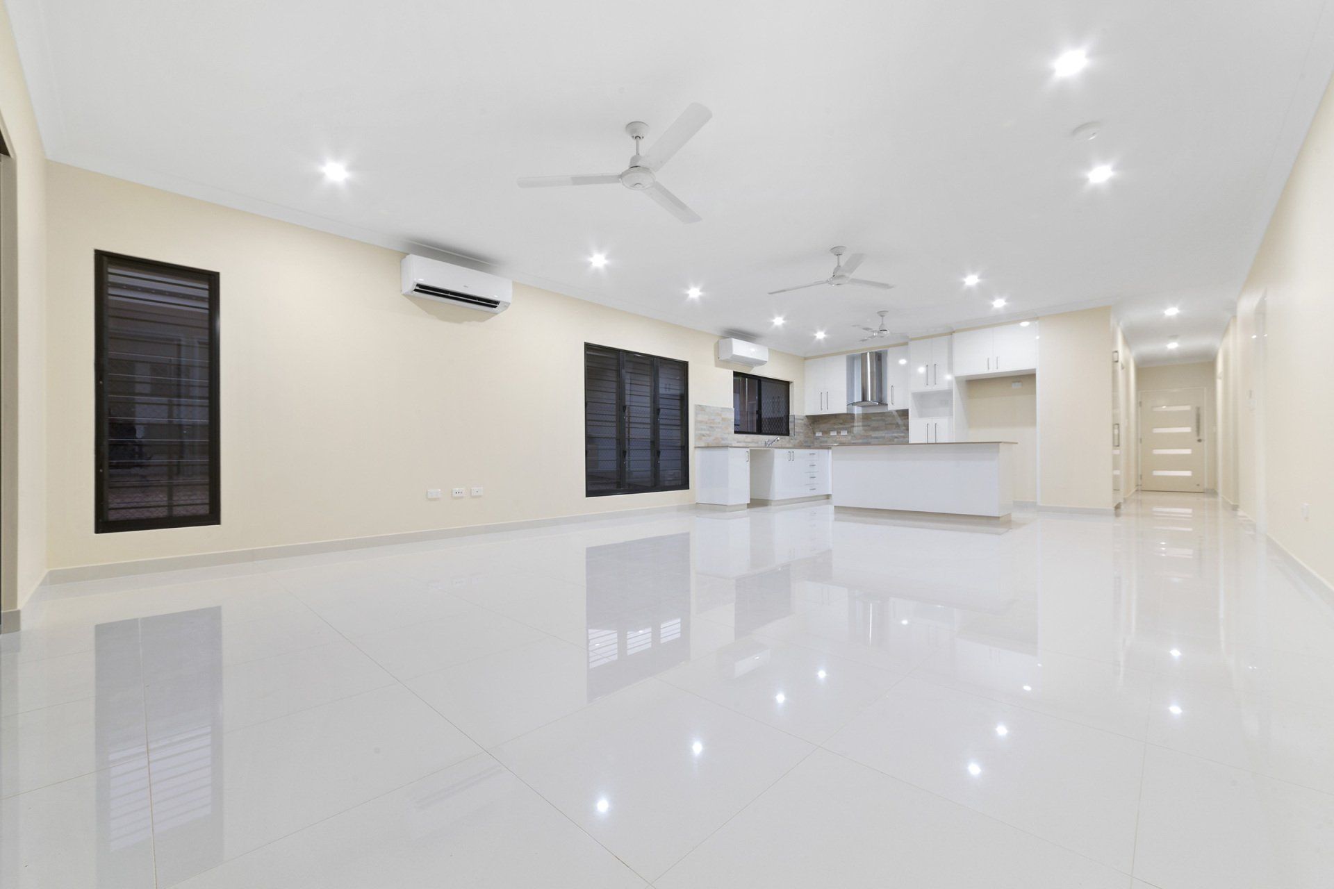 A large empty room with a kitchen and a ceiling fan.
