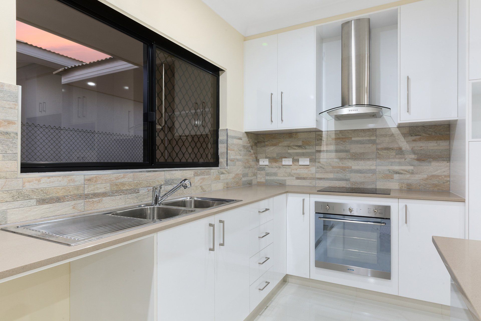 A kitchen with white cabinets , stainless steel appliances , a sink , and a window.