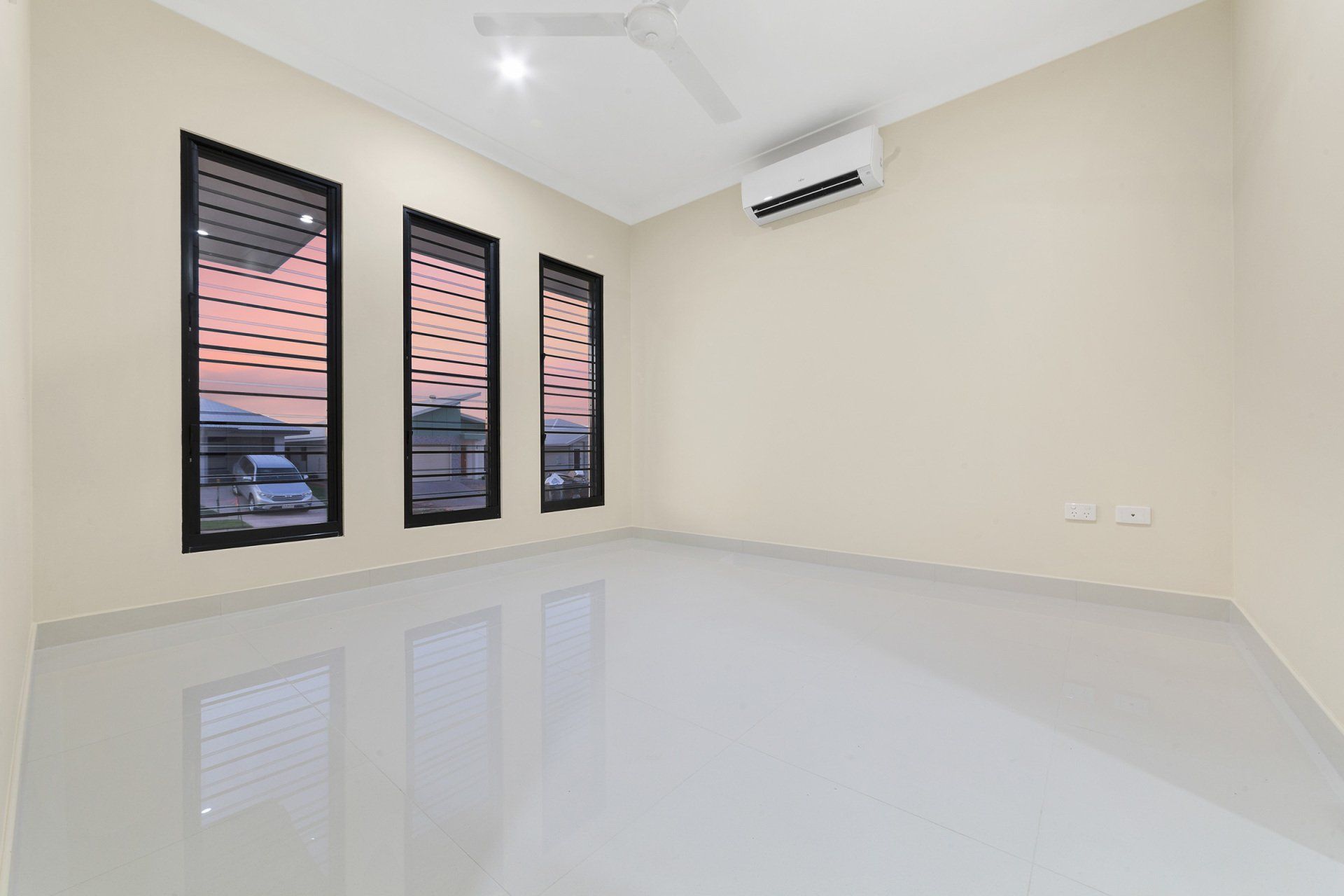 An empty room with three windows and a ceiling fan.