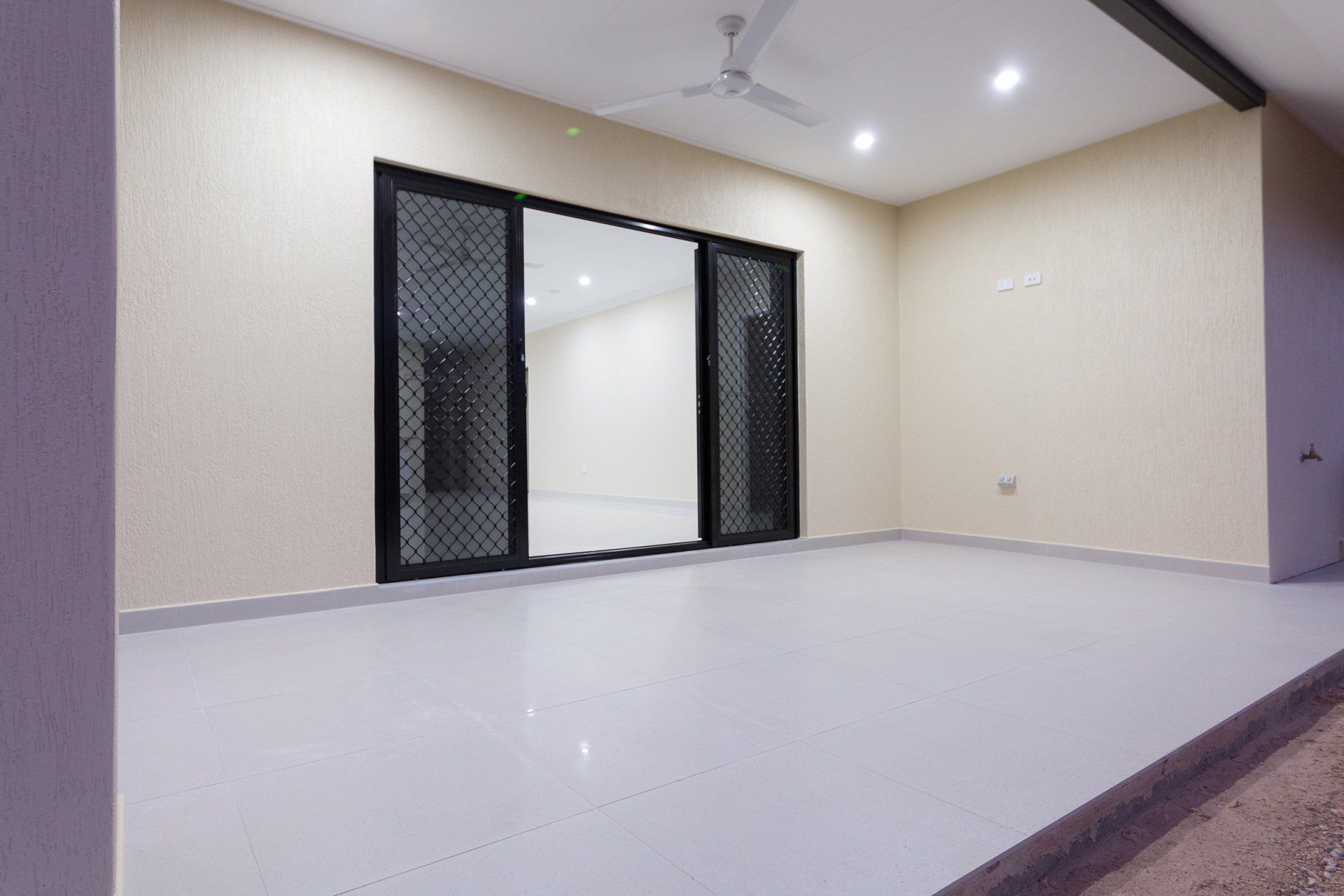 An empty room with a ceiling fan and sliding glass doors.