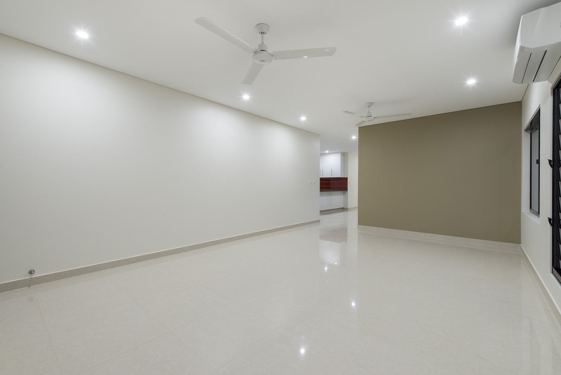 An empty living room with white walls and a ceiling fan.