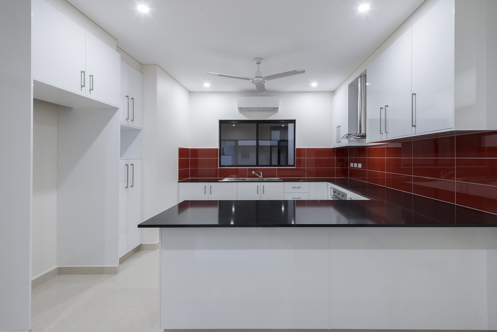 An empty kitchen with white cabinets and red tiles.