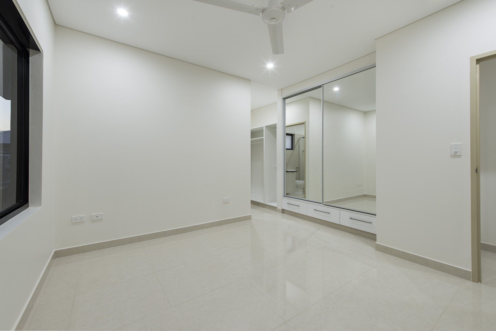 A large empty room with white walls and a ceiling fan.