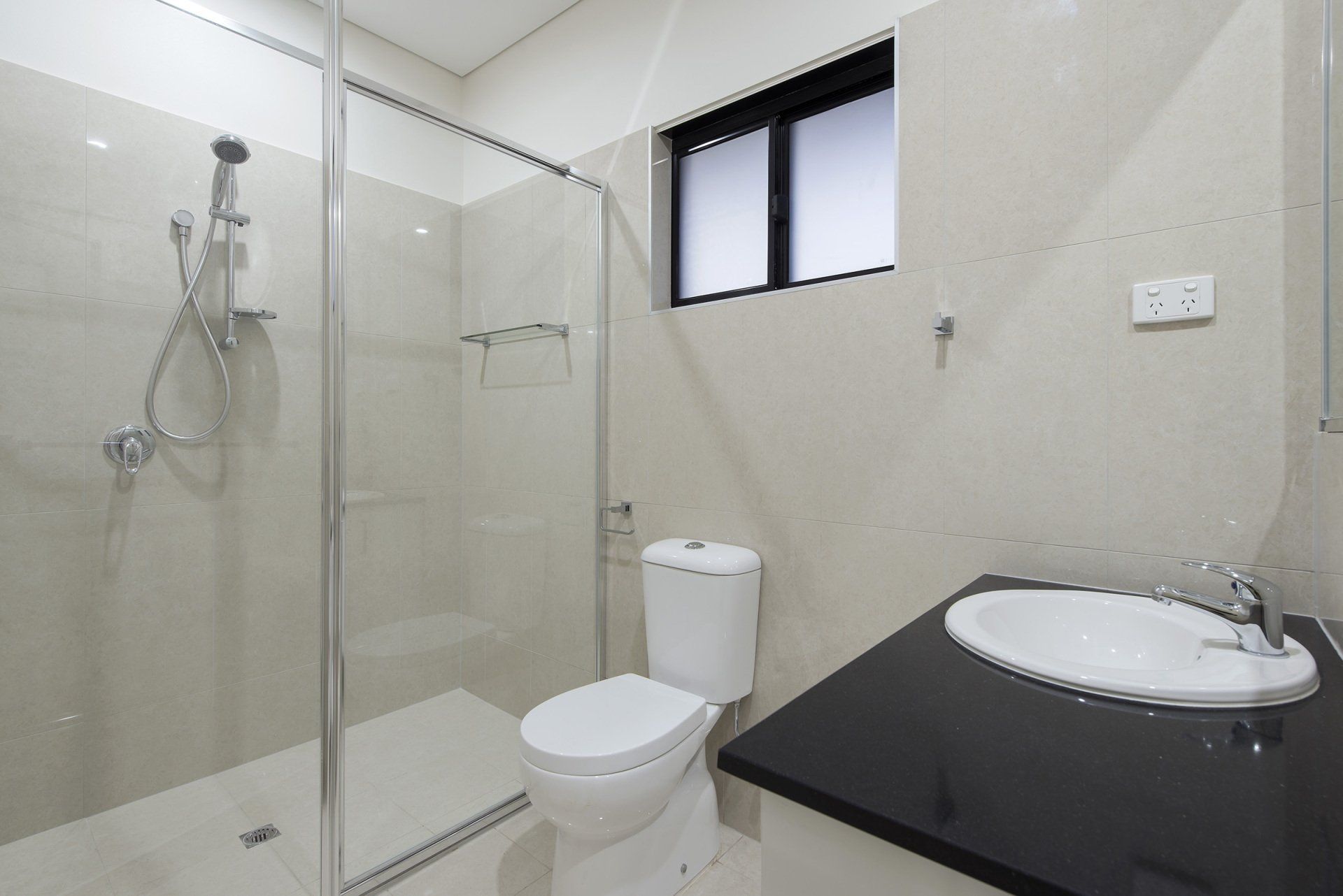 A bathroom with a toilet , sink , shower and window.