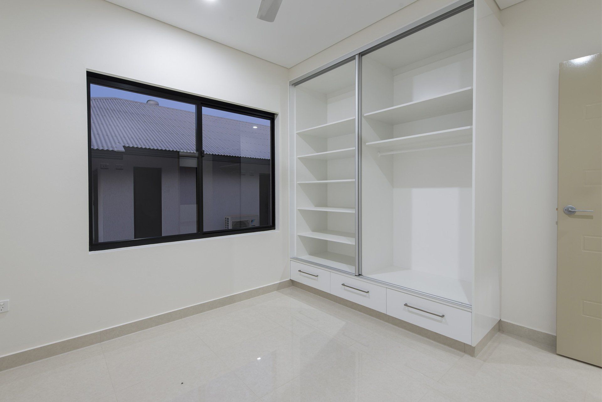 An empty bedroom with a large wardrobe and a window.