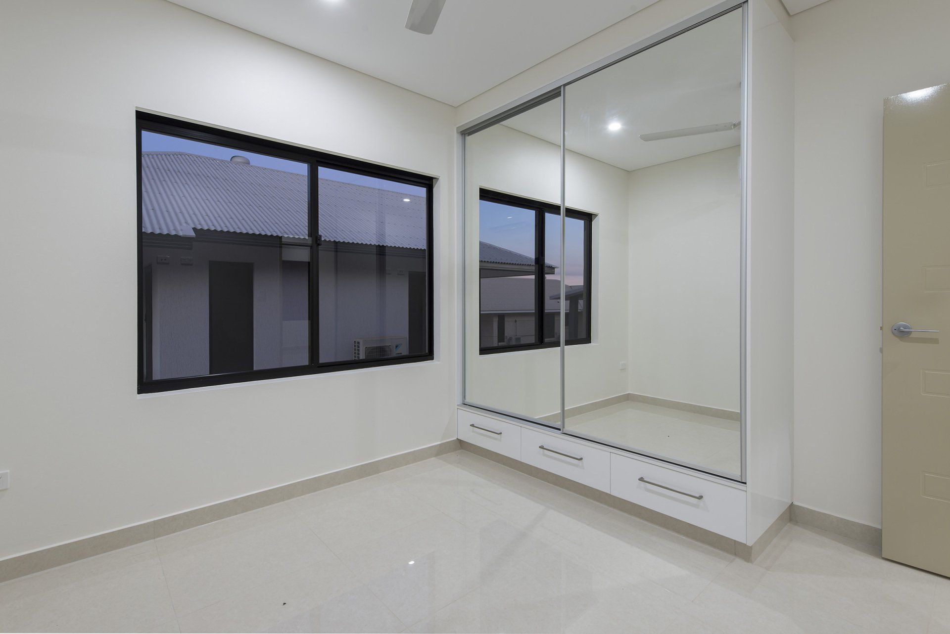 An empty bedroom with a large mirrored wardrobe and two windows.