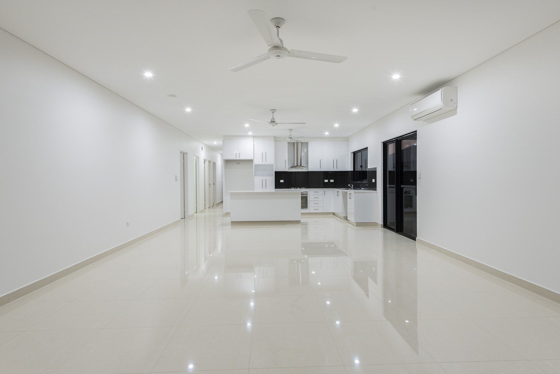 A large empty room with a ceiling fan and a kitchen.