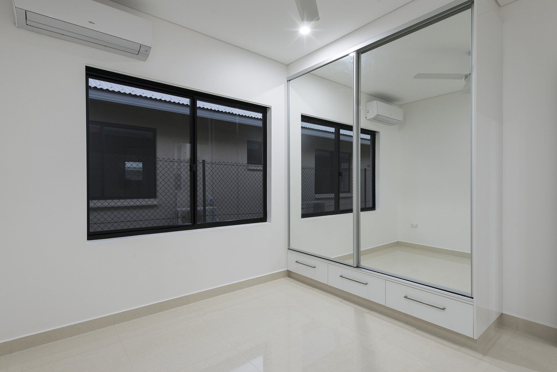 An empty room with a large mirror on the wall and two windows.