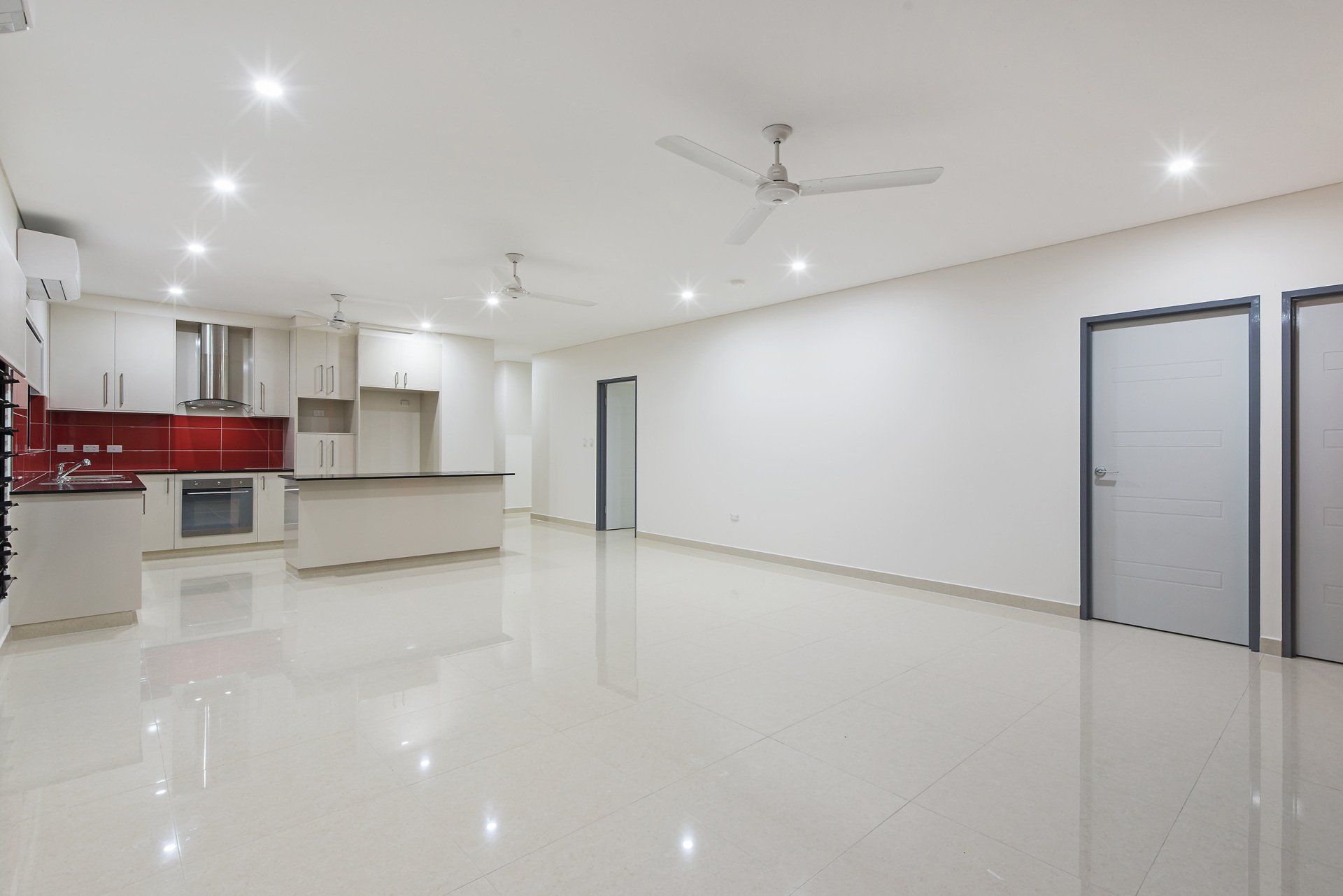 A large empty room with a kitchen and a ceiling fan
