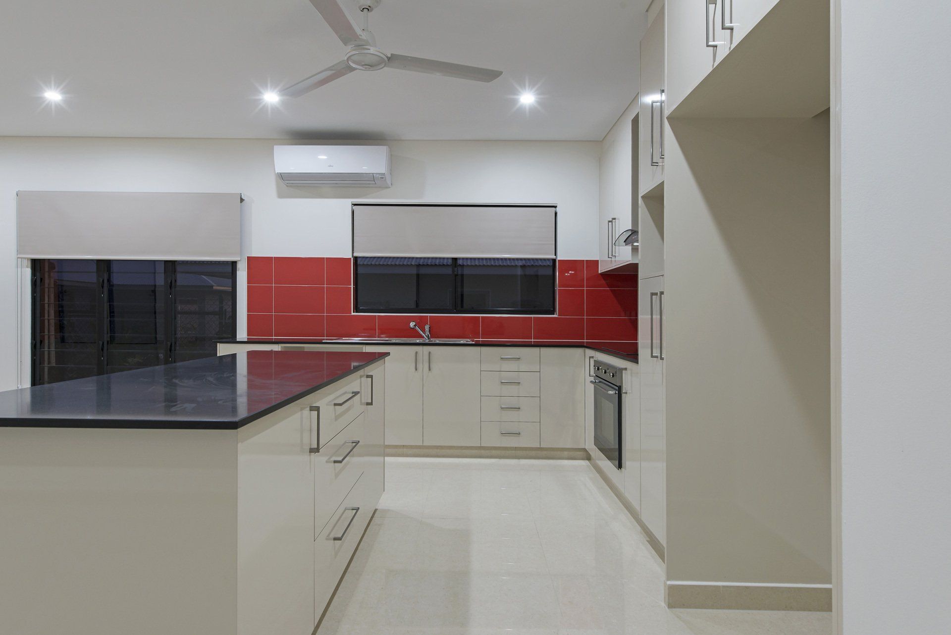 A kitchen with white cabinets and red tiles and a black counter top.