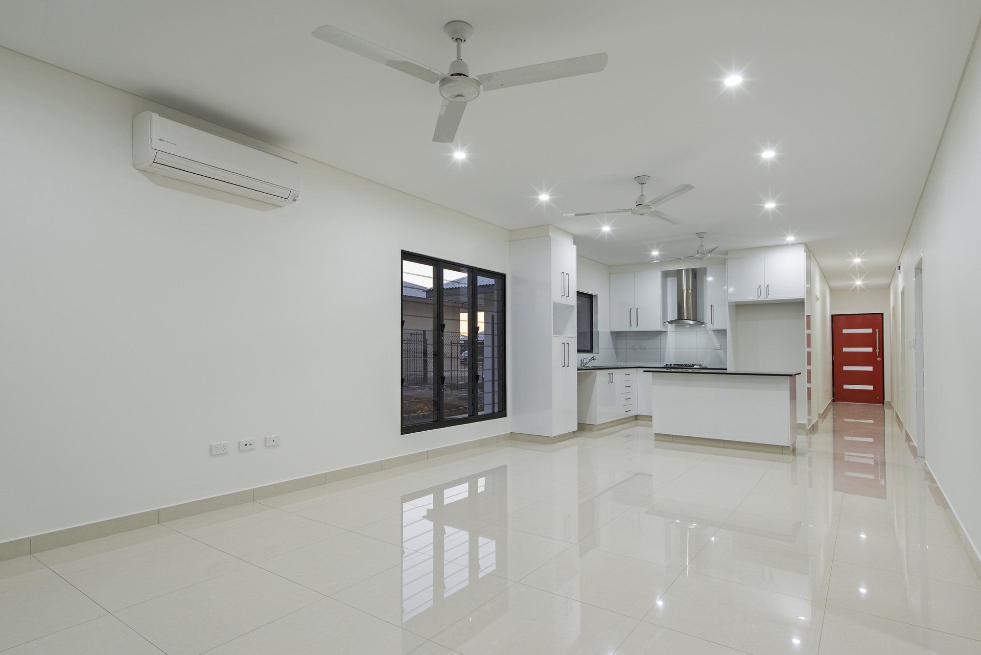 An empty living room with a ceiling fan and a kitchen.