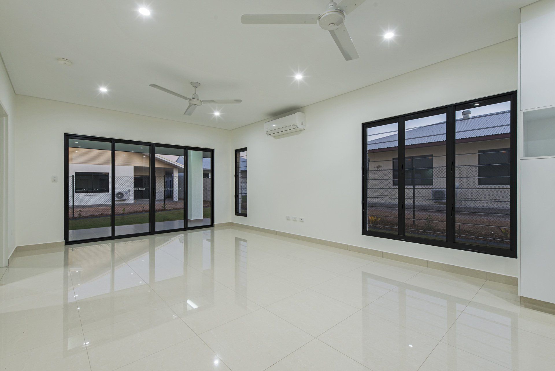 An empty living room with a lot of windows and a ceiling fan.