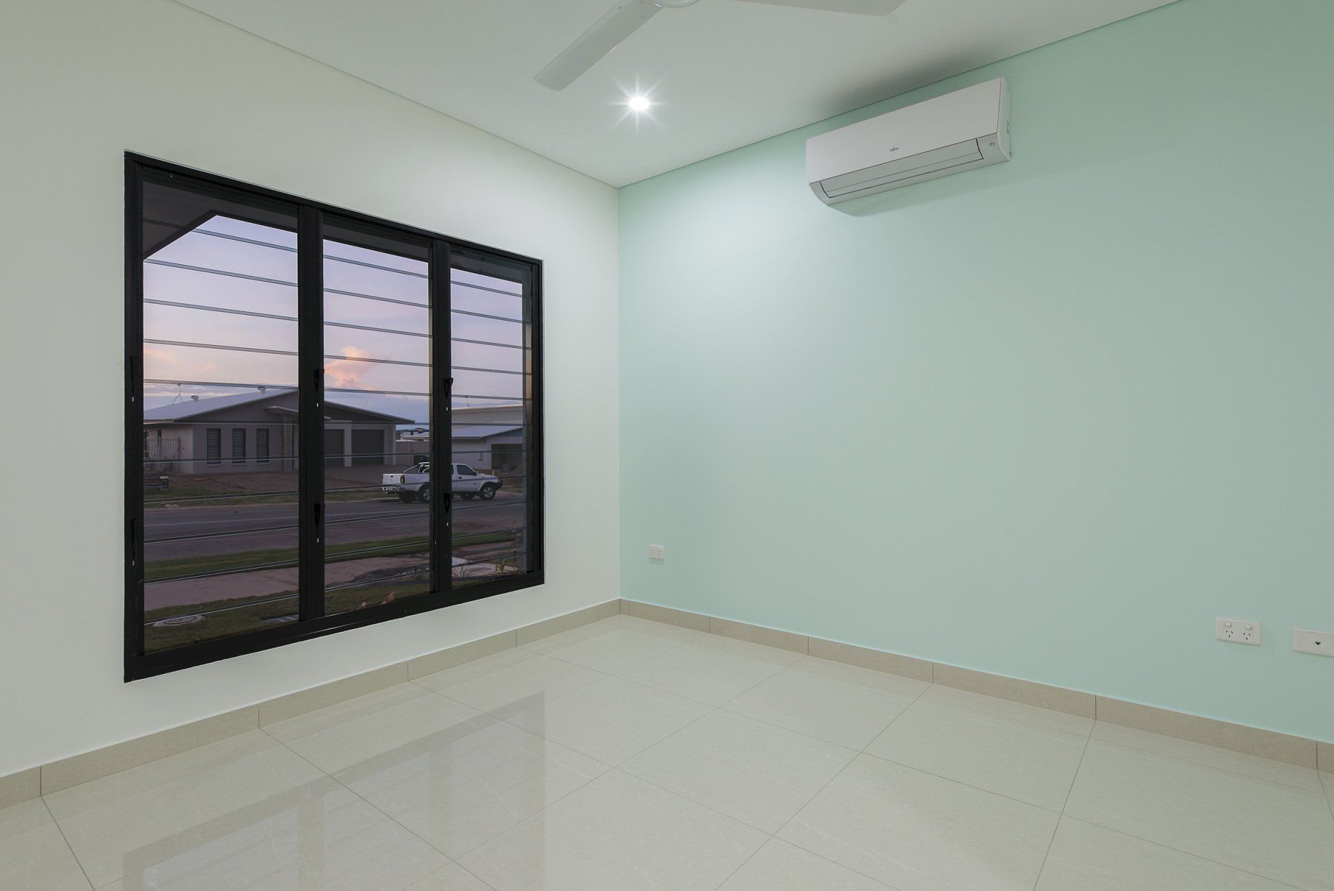 An empty room with two windows and a ceiling fan.