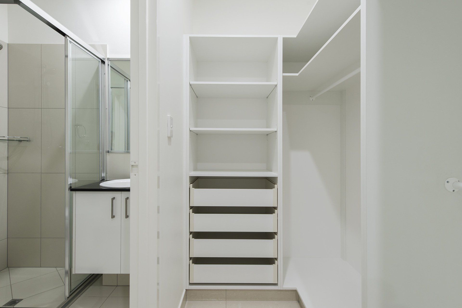 A walk in closet with drawers and shelves next to a bathroom.