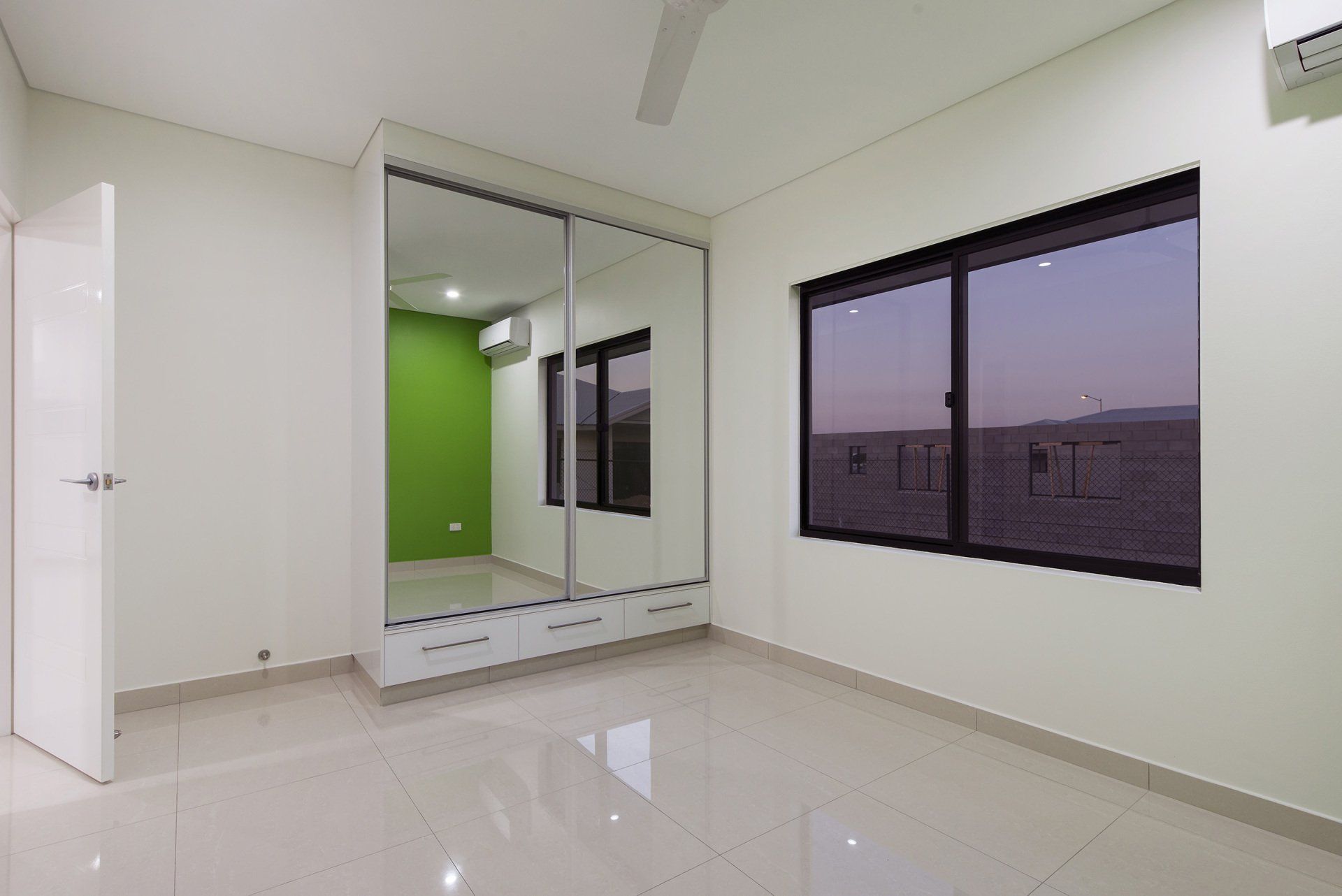 An empty bedroom with a large mirrored wardrobe and two windows.