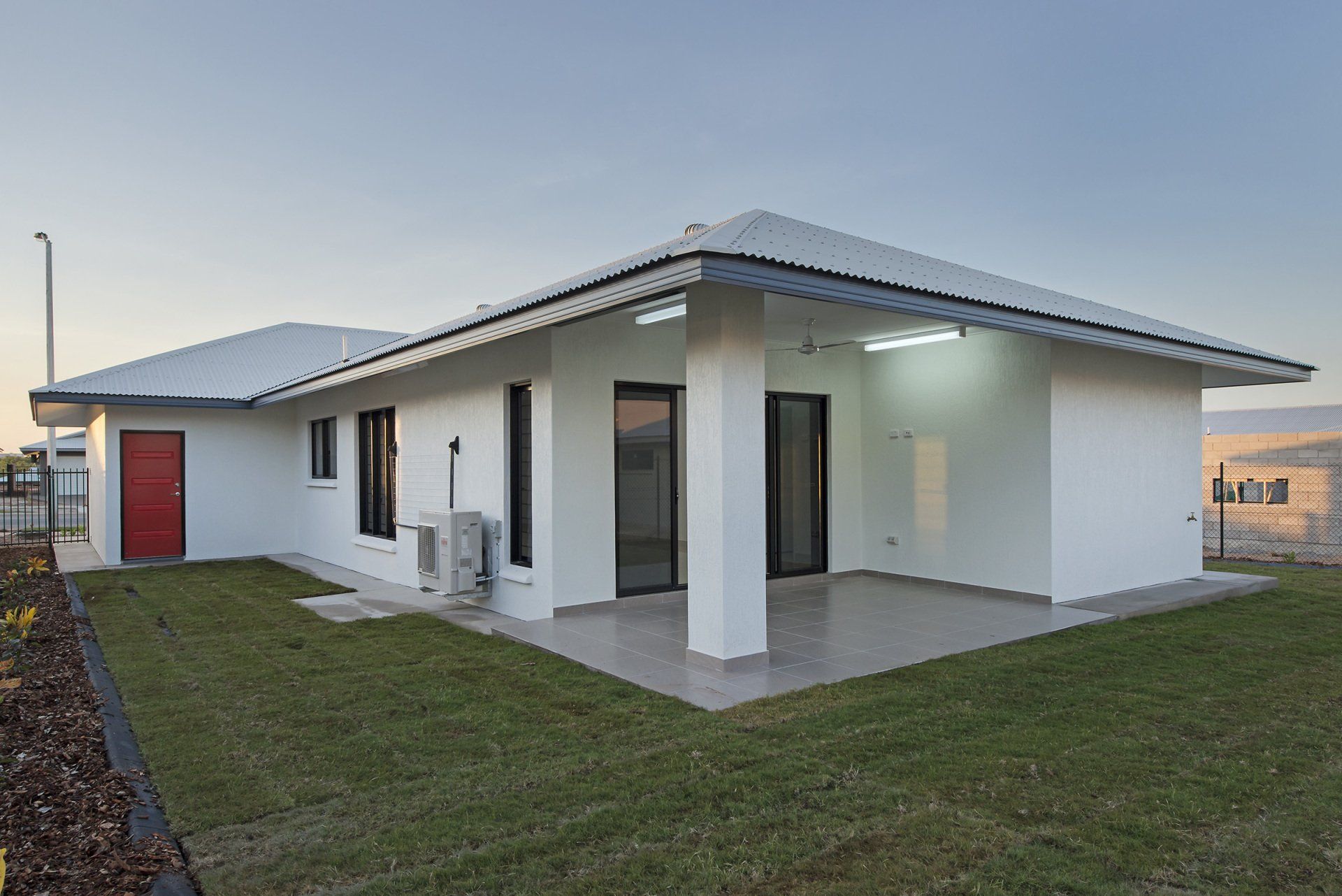 A white house with a red door is sitting on top of a lush green lawn.