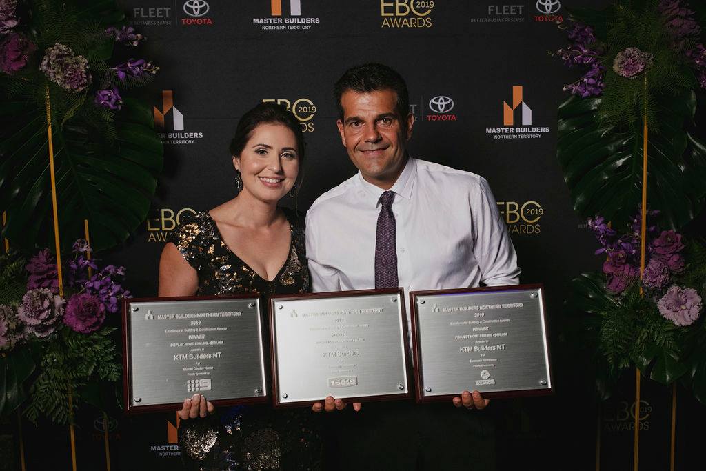 A man and a woman are standing next to each other holding three plaques.