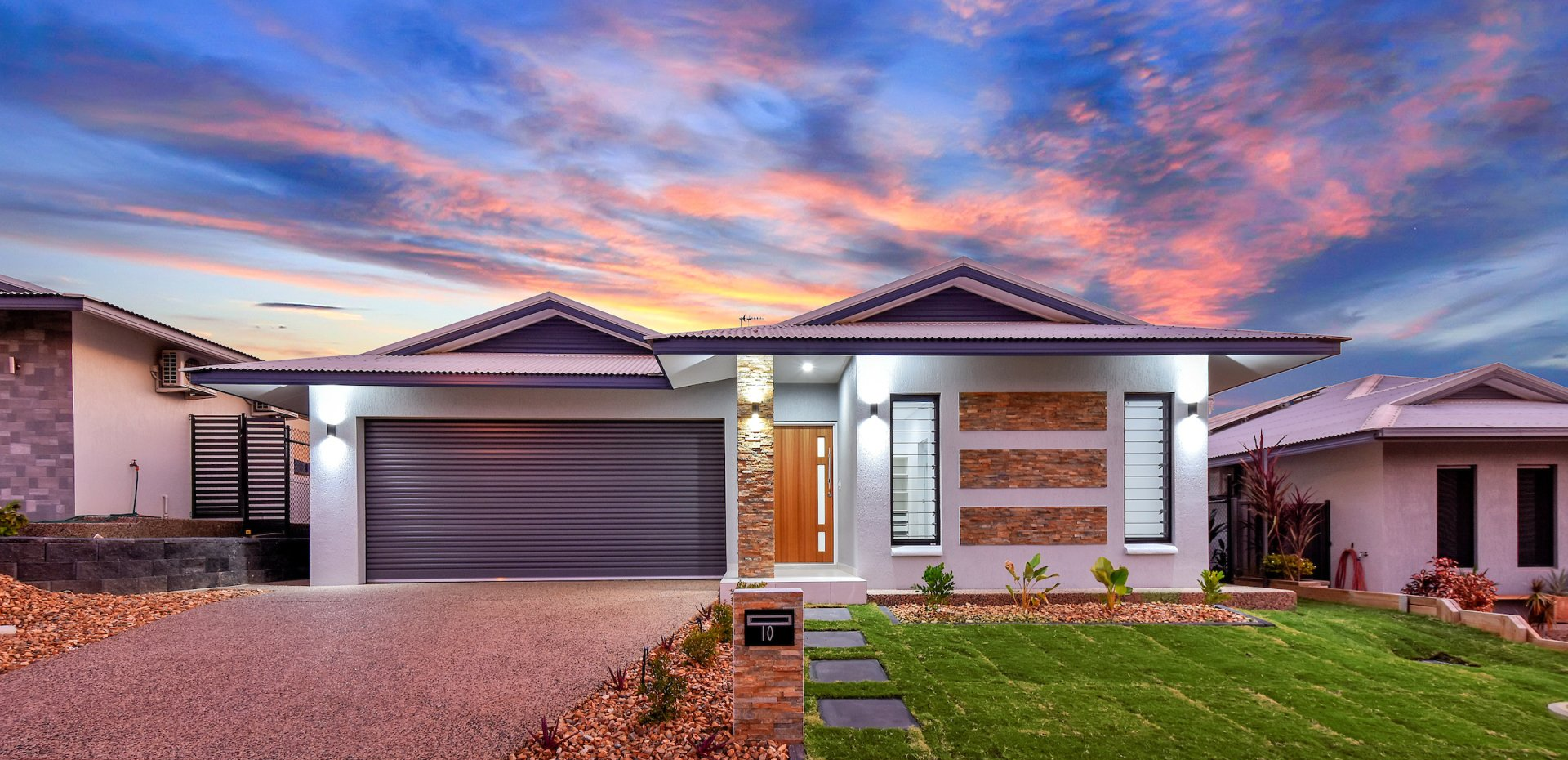A modern house with a large garage and a sunset in the background.