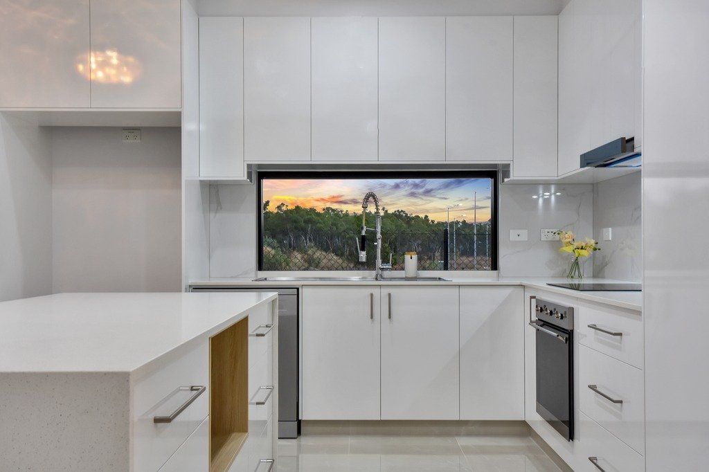 A kitchen with white cabinets , stainless steel appliances , and a large window.