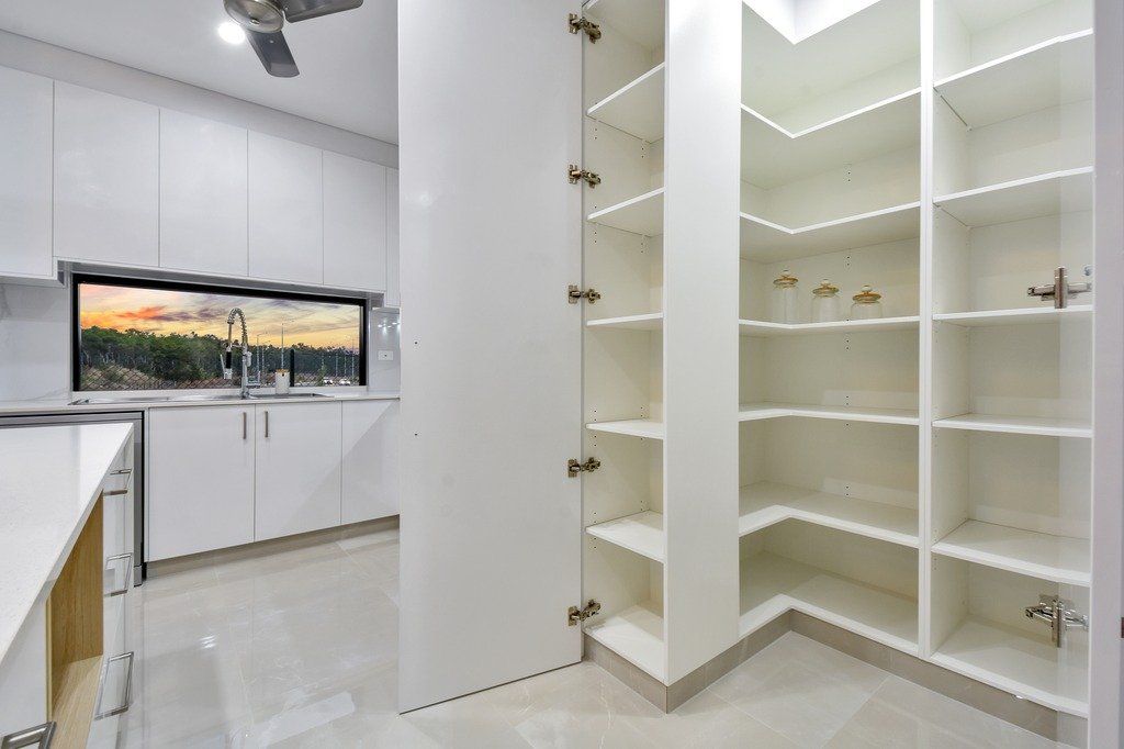 A kitchen with white cabinets and shelves and a ceiling fan.