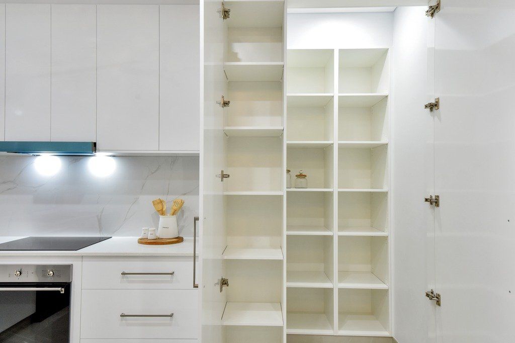 A kitchen with white cabinets and a pantry with the doors open.