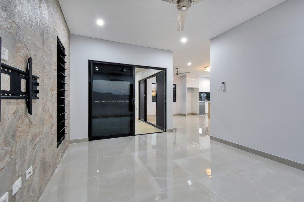A large empty room with a ceiling fan and a television mounted on the wall.