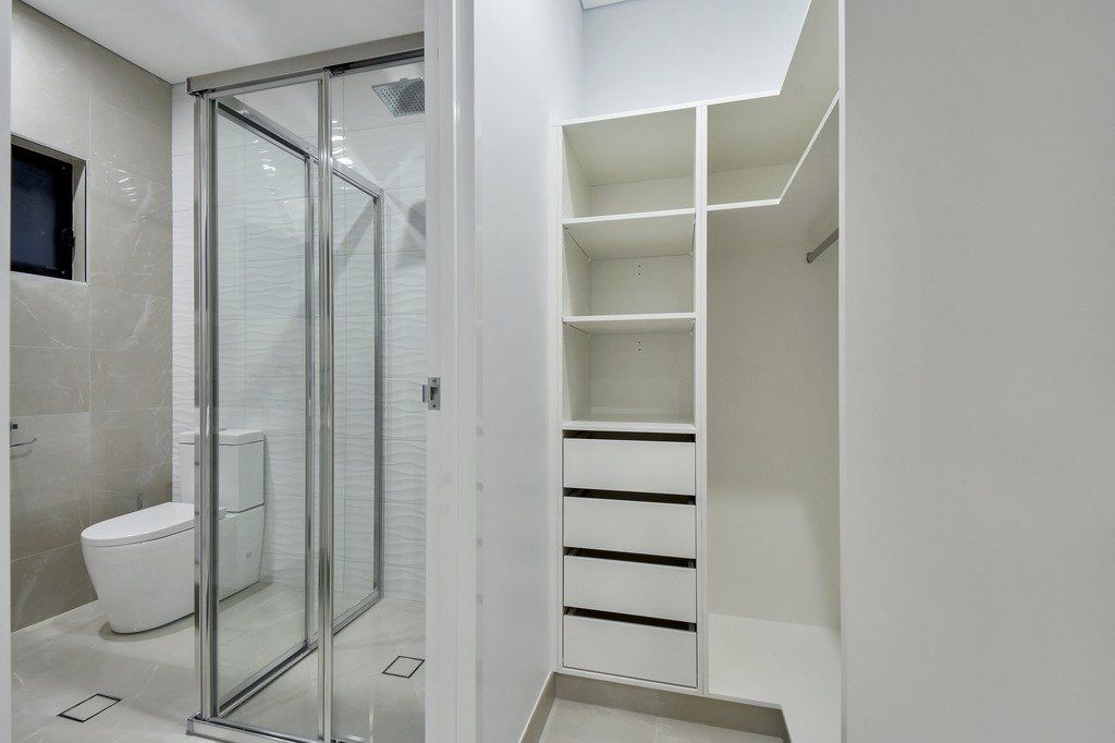 A walk in closet in a bathroom with a toilet and shower.