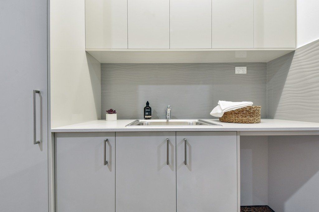 A kitchen with white cabinets , a sink , and a basket of towels on the counter.