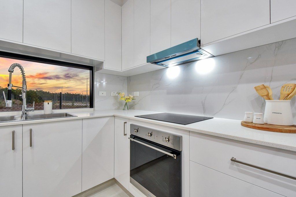 A kitchen with white cabinets , a stove , a sink , and a window.
