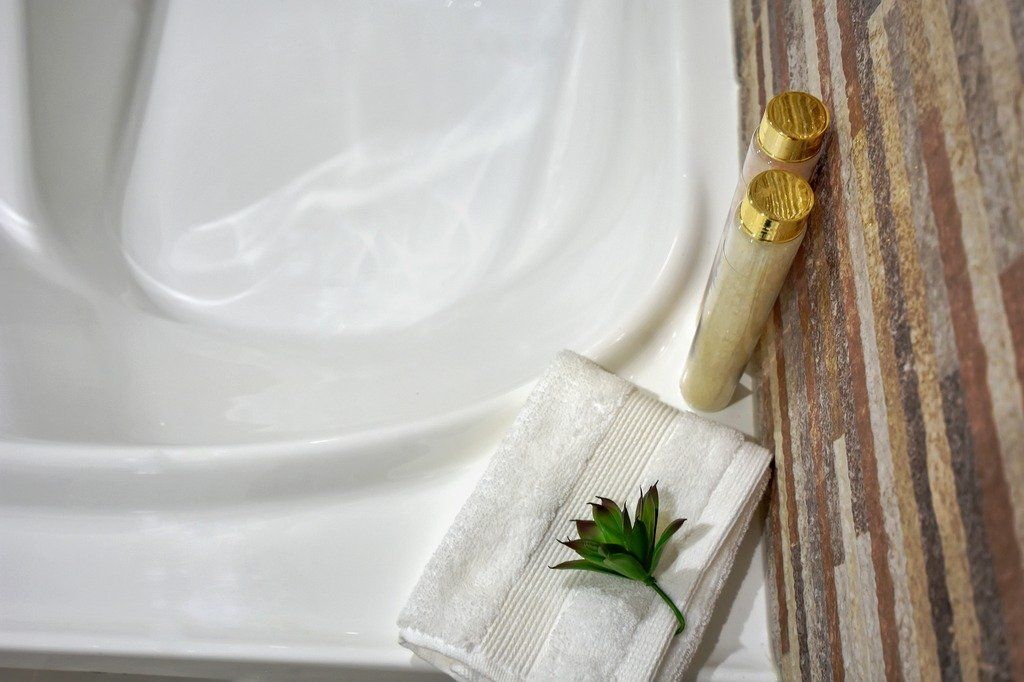 There is a towel and two bottles of shampoo on the edge of the bathtub.
