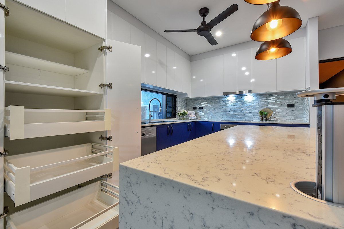 A kitchen with white cabinets and blue cabinets and a ceiling fan.