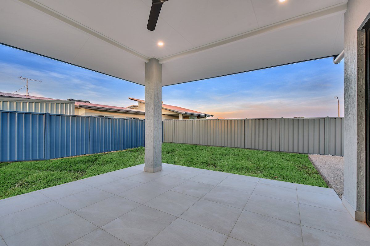 A patio with a ceiling fan and a blue fence in the background.