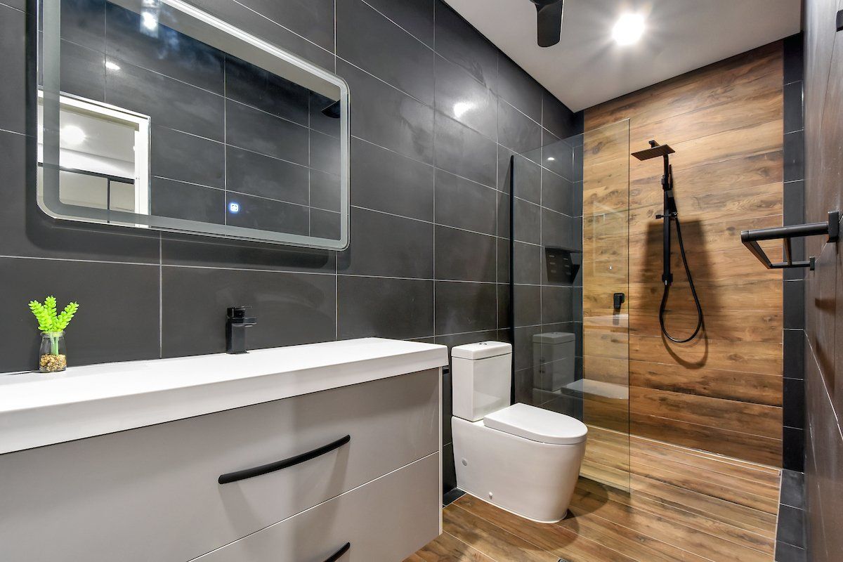 A bathroom with a toilet , sink , mirror and walk in shower.